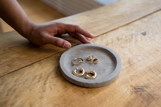 Stylish gold earrings displayed on a wooden table, featuring a hand reaching out.